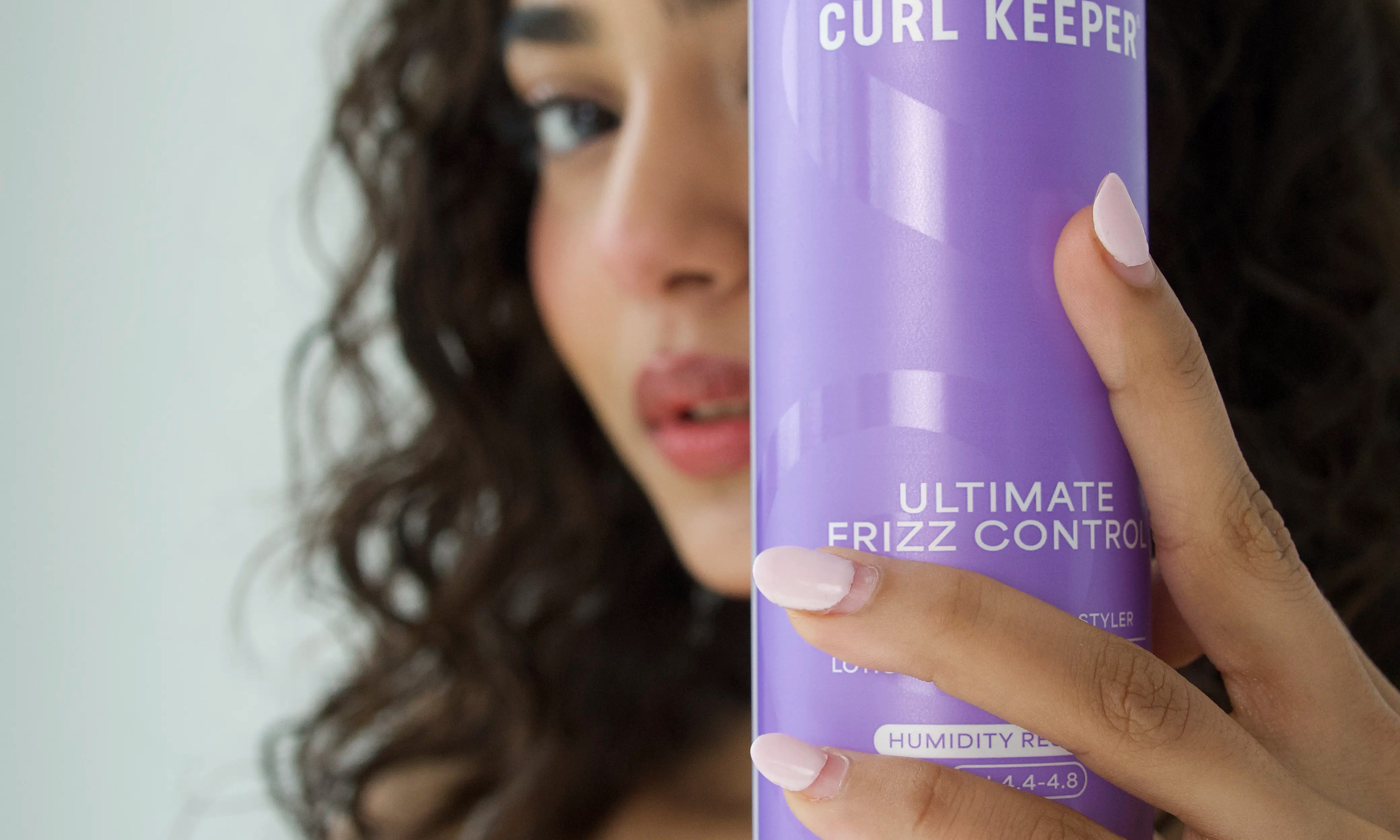 Woman with curly hair holding Curl Keepers Ultimate Frizz Control