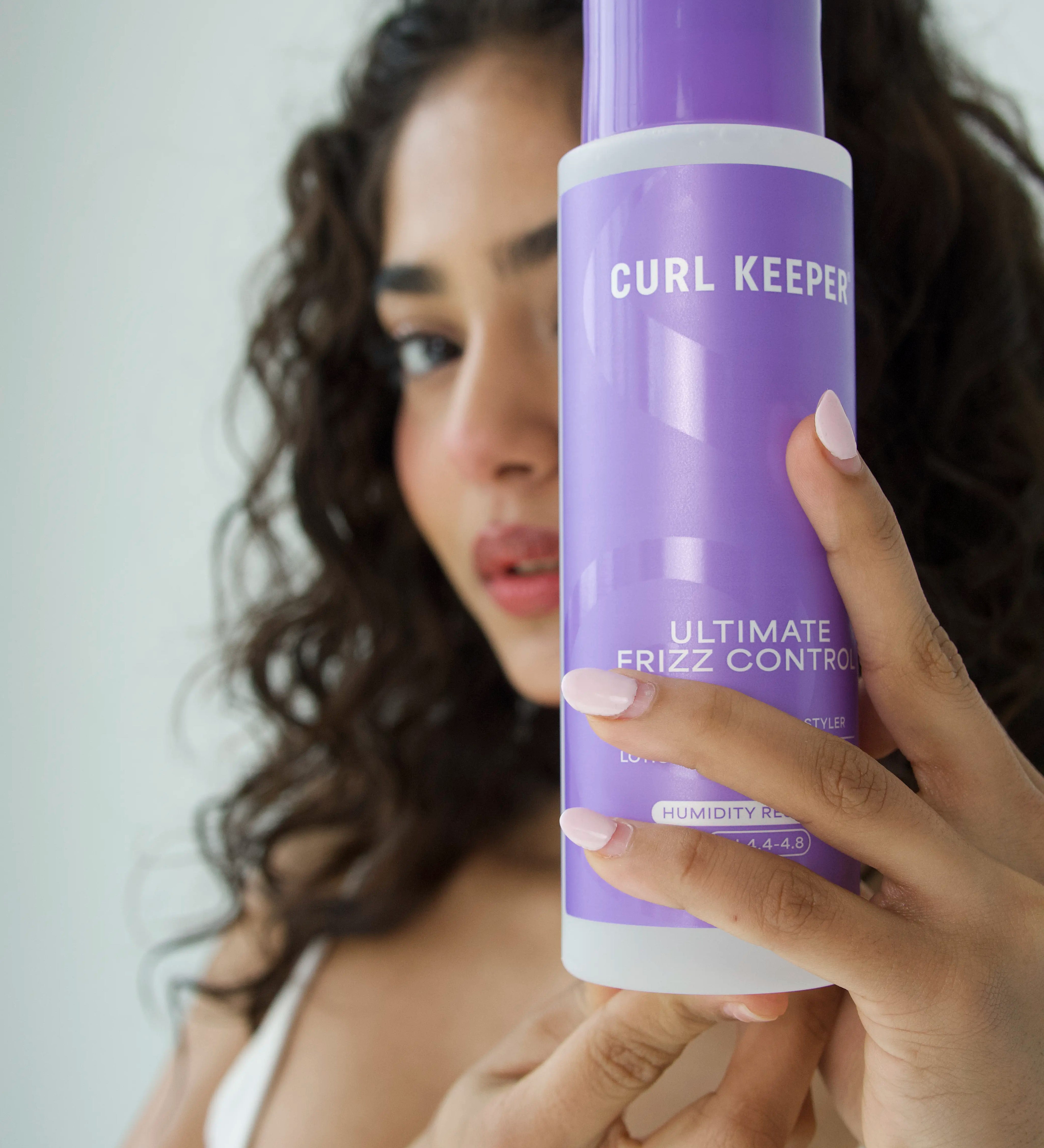 Woman with curly hair holding Curl Keepers Ultimate Frizz Control