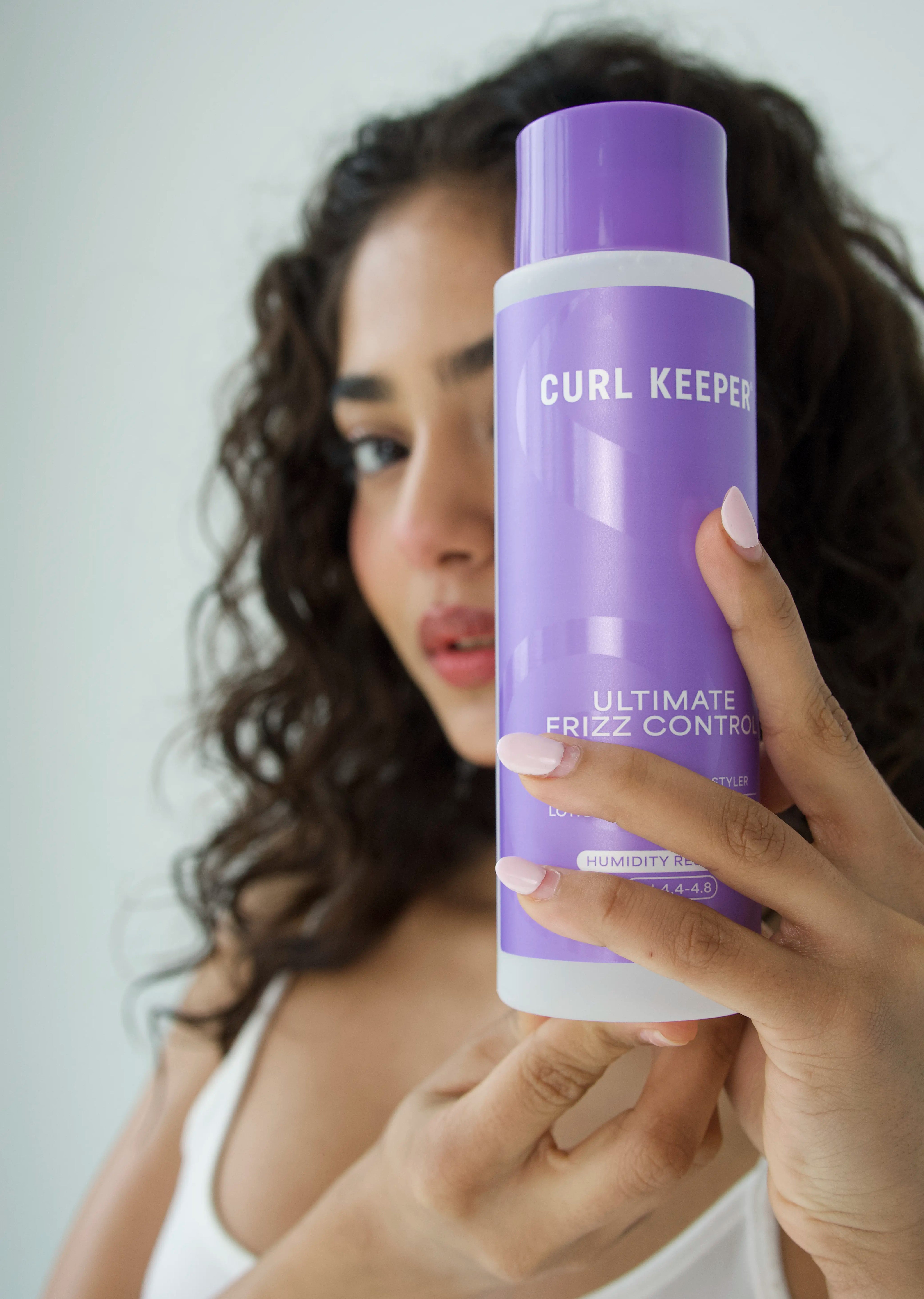 Woman with curly hair holding Curl Keepers Ultimate Frizz Control